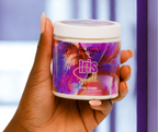Hand holding a jar of 'Iris Spell' body cream with a colorful label.
